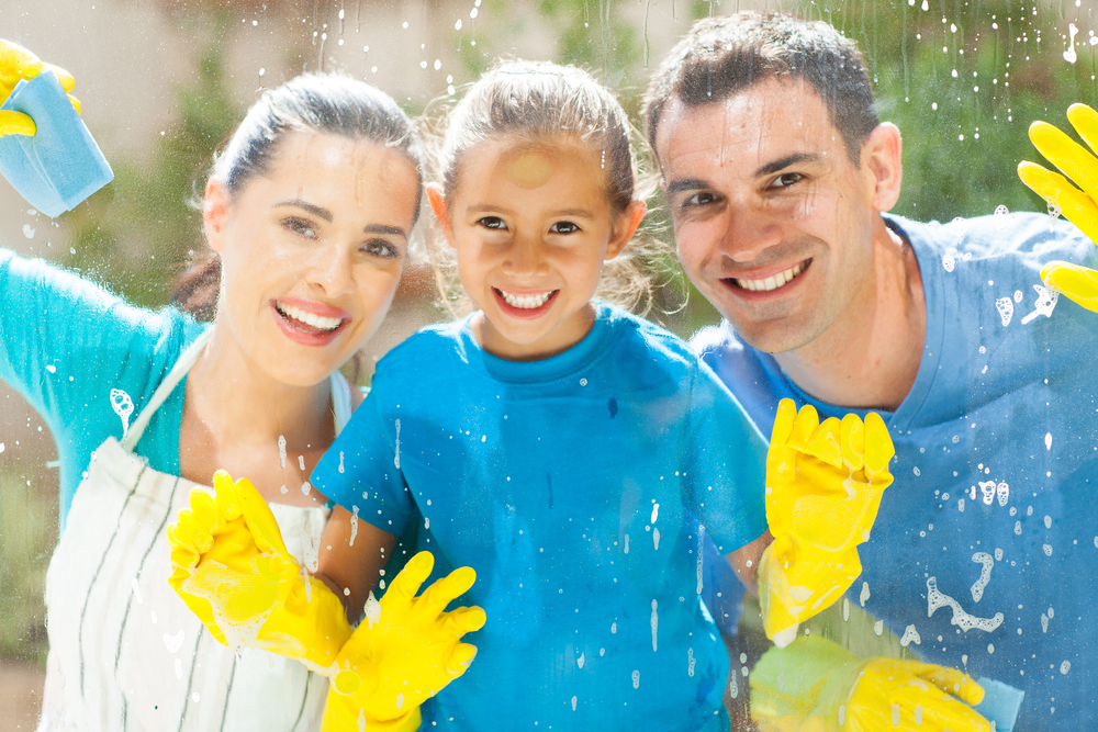 happy young family of three cleaning home window glass together